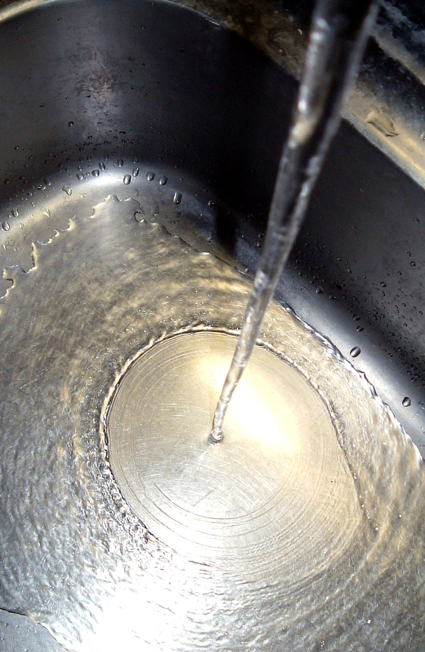 A close, slightly elevated photograph looking down into a kitchen sink, showing a sharp circular ring where a thin, fast, smooth sheet of water abruptly thickens into a slower, rougher outer ring.