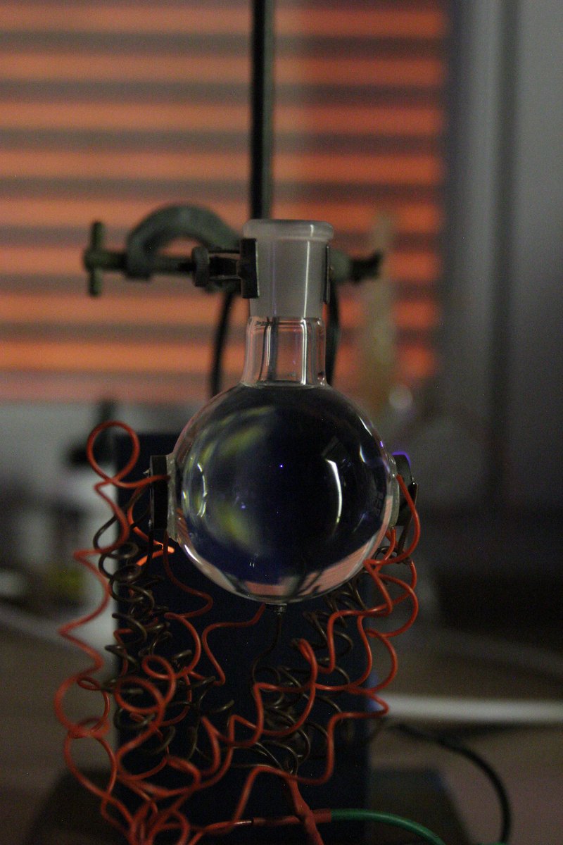 A round flask on a lab stand with a faint blue-white point of light near the centre of the water, red transducer wires coiled below